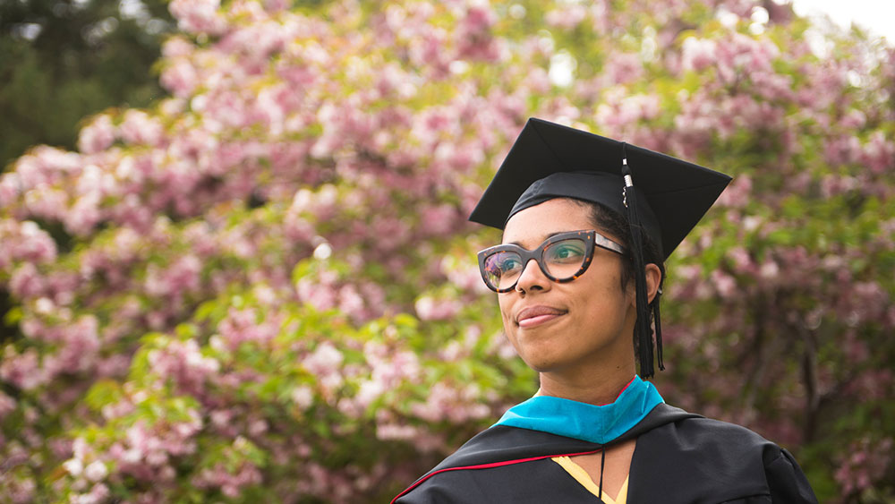 A photo of a graduate in cap and gown in front of flowers outside